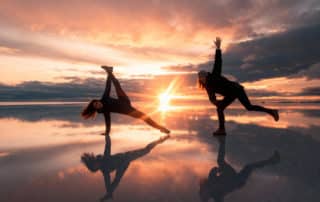Deux voyageuses posant sur le Salar d’Uyuni au coucher du soleil, reflet parfait sur le sol inondé créant un effet miroir spectaculaire.